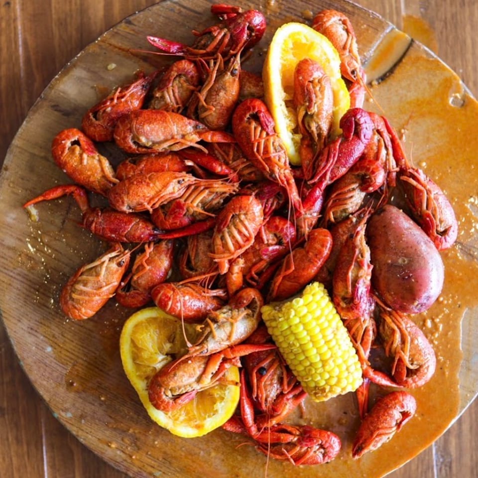 Boiled crawfish, corn on the cob, potatoes, and orange slices on a wooden platter.