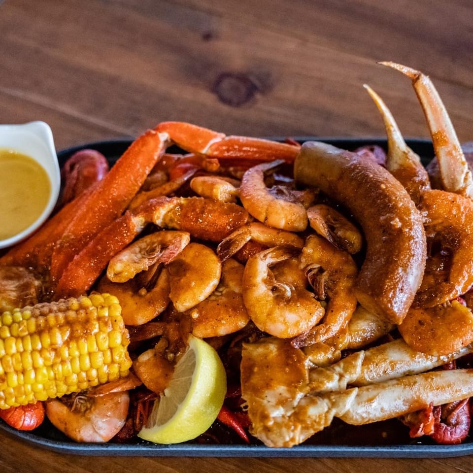 Close-up of a seafood boil with crab legs, shrimp, sausage, corn, and lemon on a dark platter.