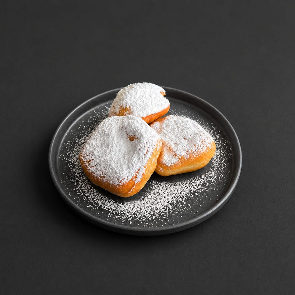 Three golden pastries dusted with powdered sugar sit on a black plate against a dark background.