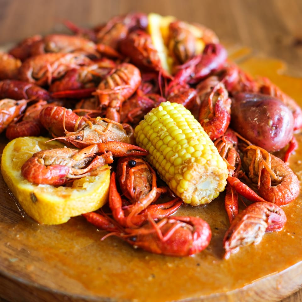A large platter of boiled crawfish, corn on the cob, and potatoes on a wooden table.